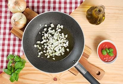 Padella con dentro olio e cipolla e si vede l’aggiunta del pomodoro e del basilico Padella con dentro olio e cipolla e si vede l’aggiunta del pomodoro e del basilico